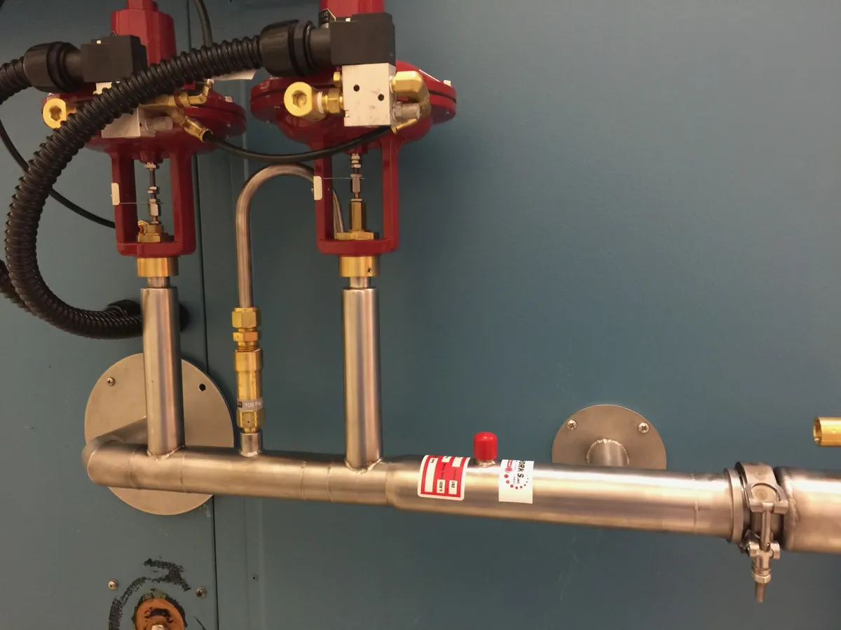 Two red vacuum-jacketed proportional LN2 valves on a vacuum-jacketed stainless manifold mounted on a chamber wall